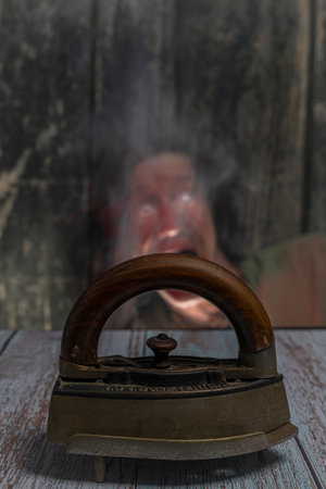Old metal iron on old wooden blue table with red male and dark smokeの写真素材