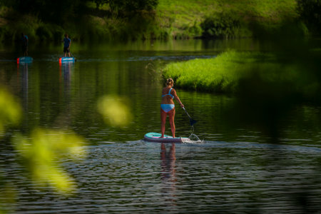 Paddle board with woman in blue swimsuit on Vltava river in hot dayの写真素材