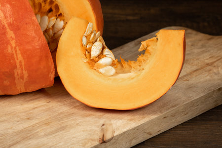 A slice of orange pumpkin with seeds lies on a wooden boardの写真素材