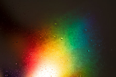 Dark glowing background with water drops with an explosion of rainbow colorsの写真素材