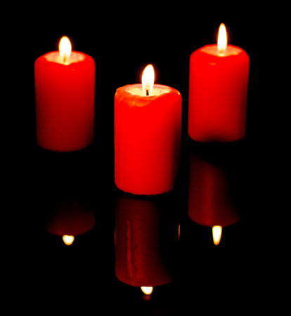Three burning red candles are reflected in a black mirror backgroundの写真素材