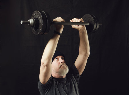 Fitness, an elderly bearded man holds a barbell in his arms straightened above his headの写真素材