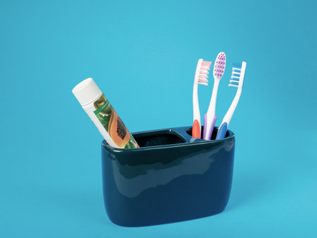Daugavpils, Latvia April 1, 2023. A set of three multi-colored toothbrushes, a tube of eco-friendly toothpaste in a ceramic container on a blue backgroundの写真素材