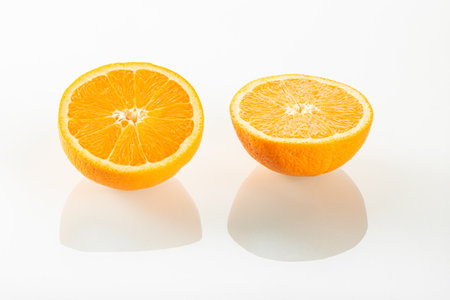 Two halves of an orange with reflection on a white mirror backgroundの写真素材