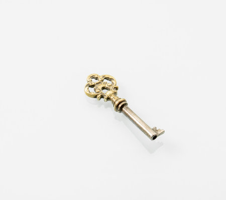 A bronze key with an ornament is reflected in a white mirror background.の写真素材