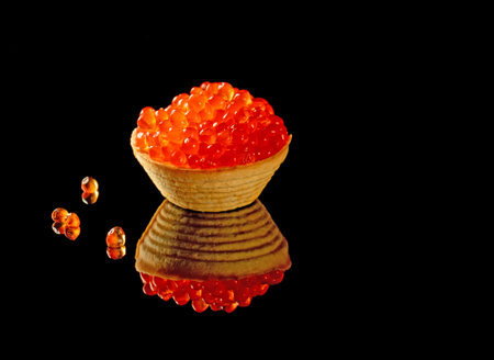 A tartlet filled to the top with red caviar is magnificently reflected in a black mirror background.の写真素材