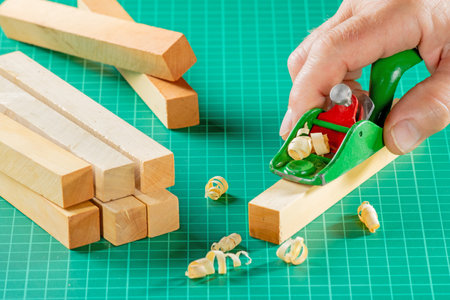 The modeler's hand cuts a block of boxwood with a miniplaner on a green model rugの写真素材