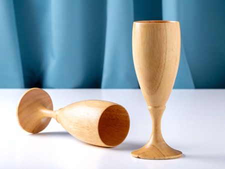 Two wooden glasses - one lies on its side, for wine on a white table against of a blue silk curtainの写真素材