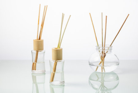 Glass bottles with incense sticks on a white mirror table.の写真素材