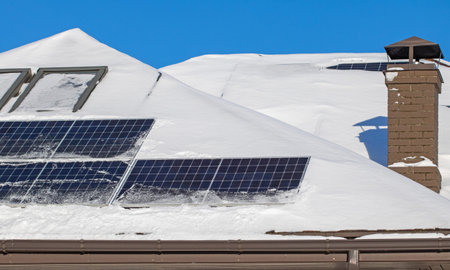 A high-angle shot of a residential rooftop with snow-cleared solar panels, providing eco-friendly...