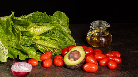 A vibrant still life composition featuring a variety of fresh, colorful vegetables including tomatoes, onions, lettuce, and avocado arranged on a dark background.の写真素材