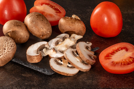 A rustic mix of fresh tomatoes and mushrooms on a dark wooden table, ideal for cooking and healthy eating concepts. The natural colors and textures make for an appealing image.の写真素材