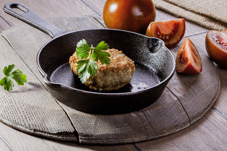 Cast iron frying pan with fried cutlet and tomatoes on wooden tableの写真素材