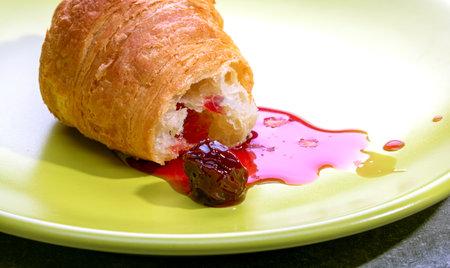 Croissant with cherry jam on a plate.
