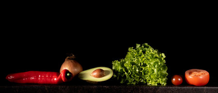 Paprika, lettuce, onion, avocado and tomato lined up on black background, low key photo.の写真素材