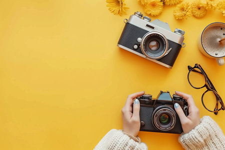 Woman holding vintage camera on yellow background with flowers and glasses, minimalist flat lay.の素材