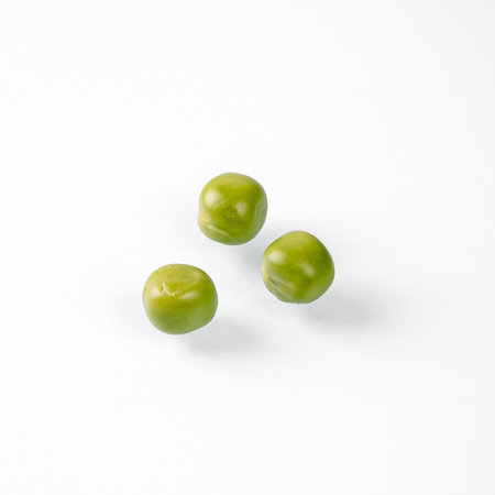 This image captures a close-up view of three vibrant green peas sitting on a pristine white...