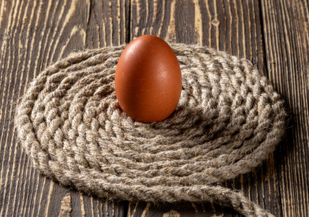 A fresh chicken egg delicately placed on a textured jute rope background, creating a rustic and natural feel. Ideal for food, farm, or organic lifestyle themes.の写真素材