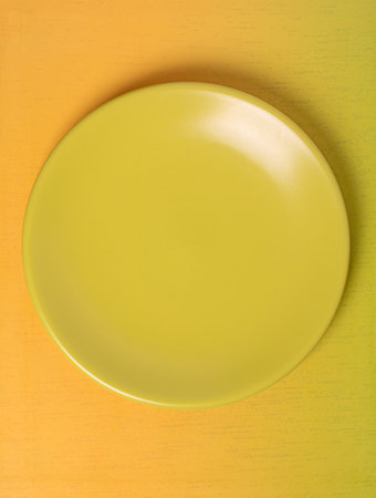 A top view of a vibrant empty yellow plate set against a visually appealing gradient background. Perfect for showcasing food, recipes, or any creative design with space for text.の写真素材