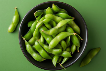Vibrant overhead shot of fresh edamame in dark bowl against bright green background for contrastの素材