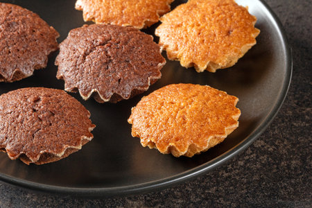 Aesthetic display of lemon and chocolate mini muffins beautifully arranged on a sleek black plate,...