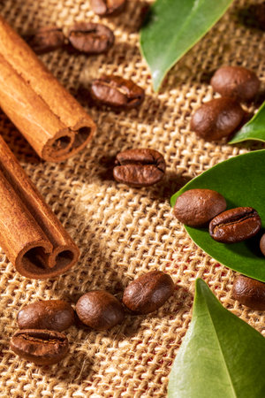 This image captures a cozy arrangement of roasted coffee beans and aromatic cinnamon sticks displayed on a beautifully textured napkin, perfect for evoking warmth and comfort.の写真素材