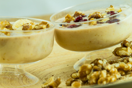 Two smoothies one with dried cherries and crushed walnuts and the other with sliced banana fruit on topの写真素材