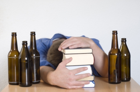 Young student passed out behind books. Surrounded by empty beer bottles.の写真素材