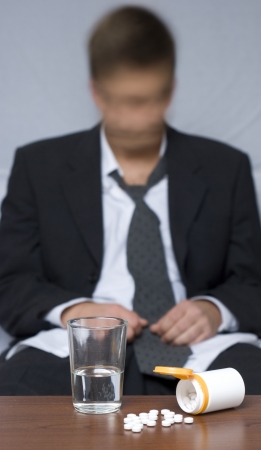 Businessman sitting on the floor. Pills on the table. Blurry and out of focus background.の写真素材