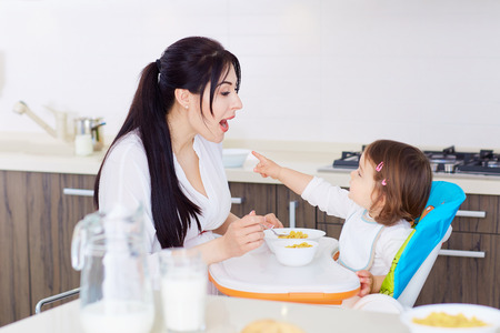 Mum spoon feeding child in kithenの写真素材