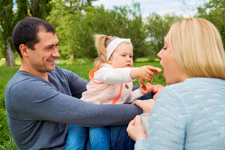 Happy family picnicking in the park. Daughter feeding mother playfully.の写真素材