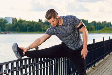Male runner doing stretching exercise, preparing for workout in the park.の写真素材