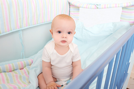 Cool kid sitting in baby bed and look.の写真素材