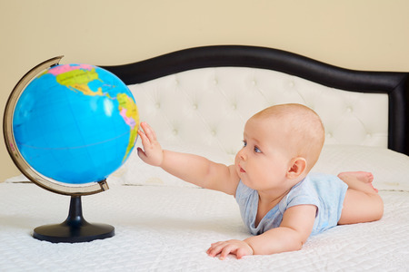 The concept of peace, protection, childhood. Baby boy,child, toodler playing with a globe on a bed in a room inside the building.の写真素材