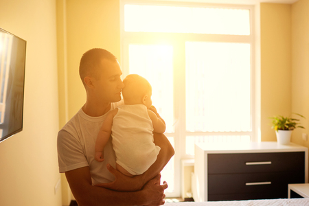 Son on father's hands at the window in the morning sun. The concept of parenthood, child protection.の写真素材