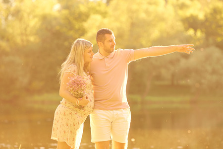 Pregnant couple in the rays of sunlight at sunset. Husband hugs his pregnant wife tenderly. The concept of a happy family, love and pregnancy.の写真素材