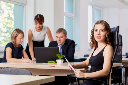 Portrait of curly business woman in the office in a chair on the background of working business partners.の写真素材