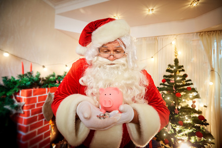 Santa Claus holding a pig piggy bank and coins in Christmas.の写真素材