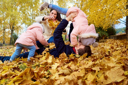 Happy family lying on the yellow leaves in the park playing actively in the autumn, fooling around, having fun. The concept of a happy family.の写真素材