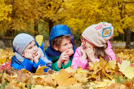 Group of children lying in a park on yellow leaves in autumn park on nature.の写真素材