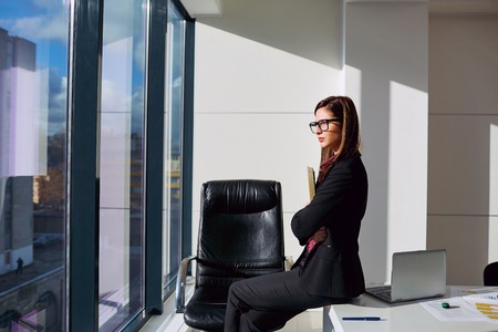 Business woman with glasses looking through a window in  modern business office.の写真素材