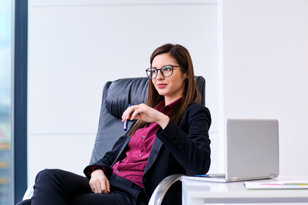 Business woman with glasses looking out of the window while sitting at your desk in officeの写真素材
