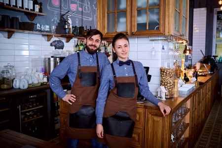 Two workers bartender barista girl and a man at work behind the bar in restaurant laughing, smiling.の写真素材