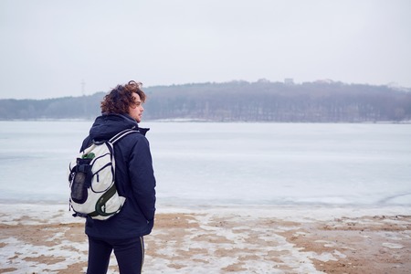 The curly haired man in a jacket with  backpack   winter at  lake travels.の写真素材