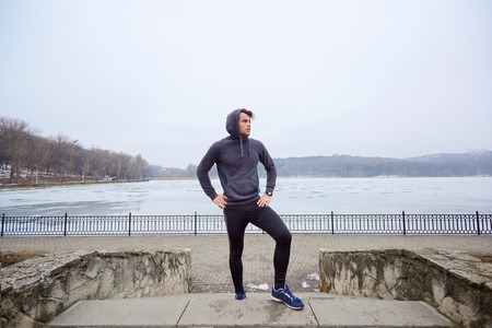 Young man in sports clothing on steps the park against  backdrop of a frozen lake in  spring.