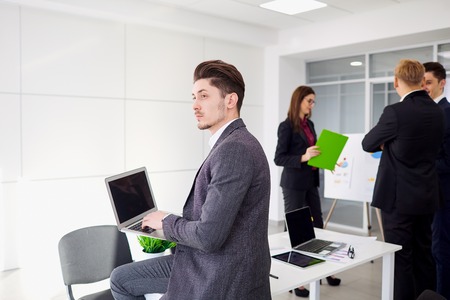 Young businessman with a laptop in the hands of works in  background colleagues  office.