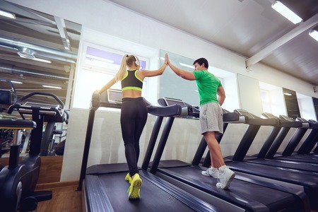 Personal trainer man with athletic girl on a treadmill in the gym.の写真素材