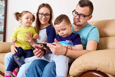 Happy family is sitting with a tablet in the room on the couch.の写真素材