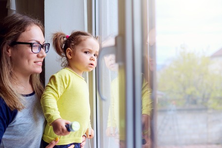 A happy family. Little girl looks out the window with mother.の写真素材