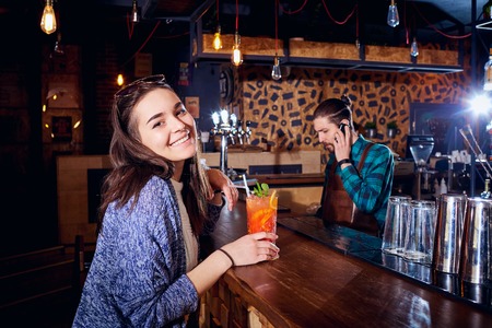 A girl with  cocktail smiles behind counter at the bar.の写真素材